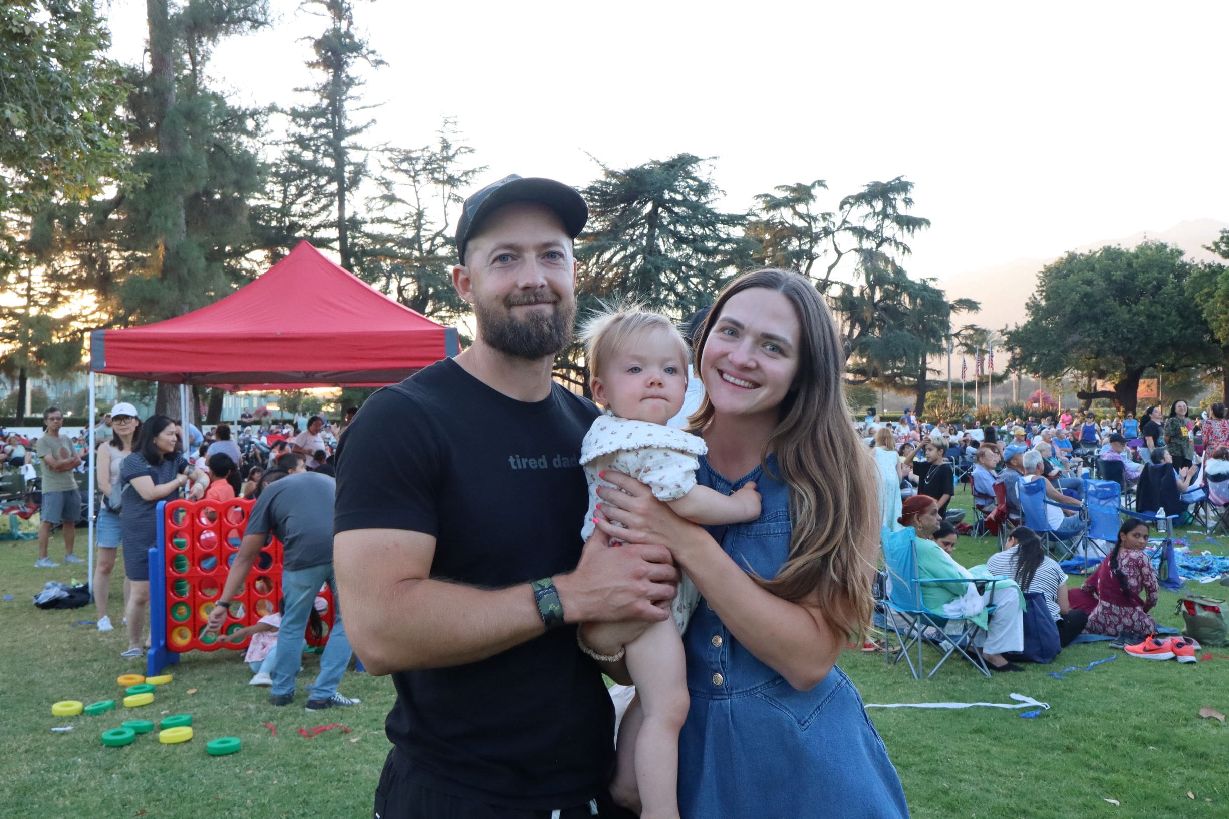 A man and a woman holding their infant child between them at an outdoor event in the park